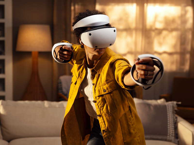 Person wearing VR headset and yellow jacket with arms outstretched in modern interior space.