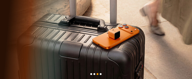 Black hardside luggage with orange smartphone holder mounted on top.