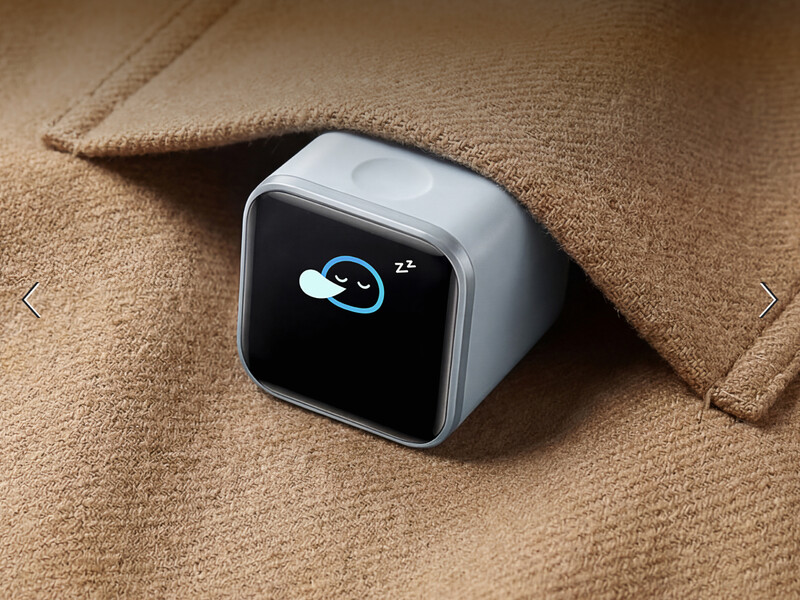 Compact white smart device with blue sleep mode icon displayed on black screen, resting on beige fabric.