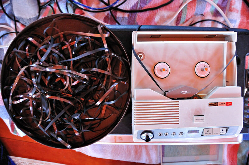Vintage tape machine with tangled red and blue cables spilling from an open reel compartment.