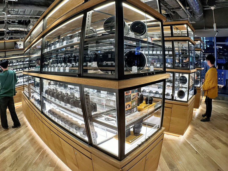 Modern retail display case with illuminated shelving showcasing camera equipment and accessories.