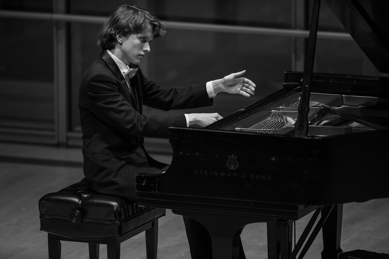 Pianist in formal attire performing at a grand piano in black and white.