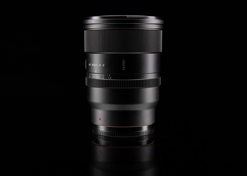 Black telephoto lens with textured grip sections and focus ring against dark background.