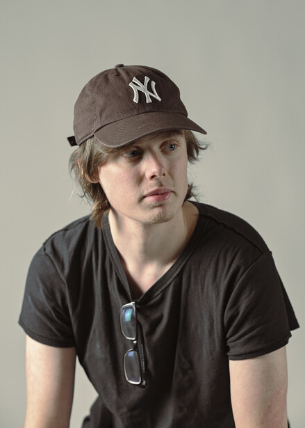 Person wearing a dark v-neck t-shirt and Yankees cap against a neutral gray background.
