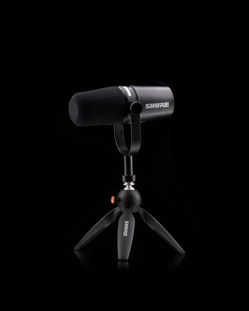 Shure SM7B microphone mounted on a compact tripod stand against a black background.