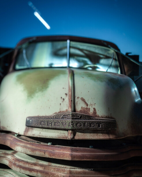 Weathered vintage car hood and grille photographed at night under a starry sky.