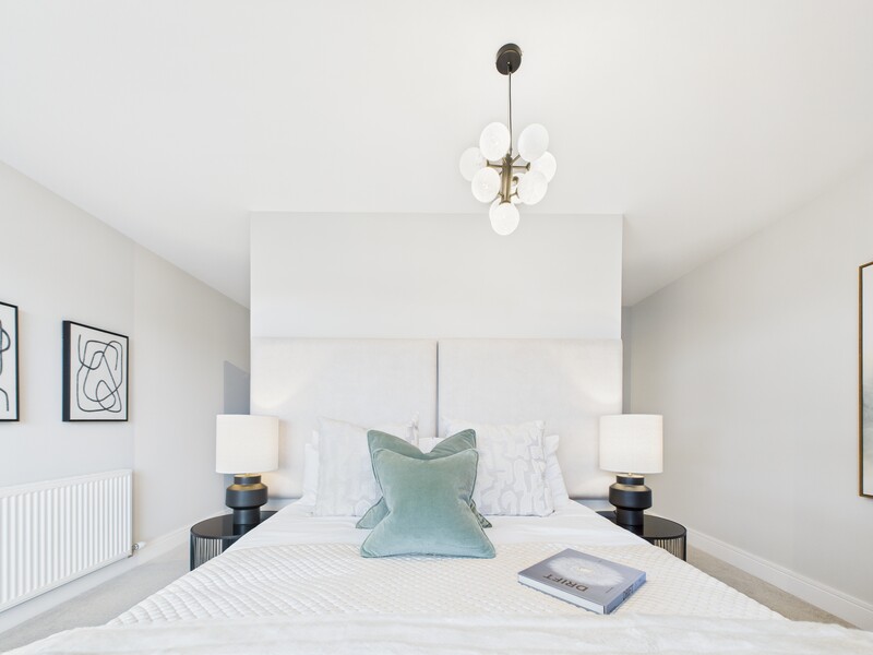 Minimalist bedroom with white headboard, symmetrical nightstands, and sage green accent pillow centered on bed.