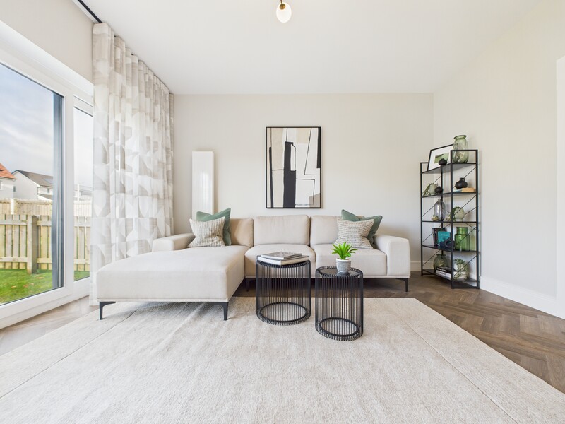 Bright minimalist living room with cream sectional sofa, black side tables, and large windows overlooking a garden.