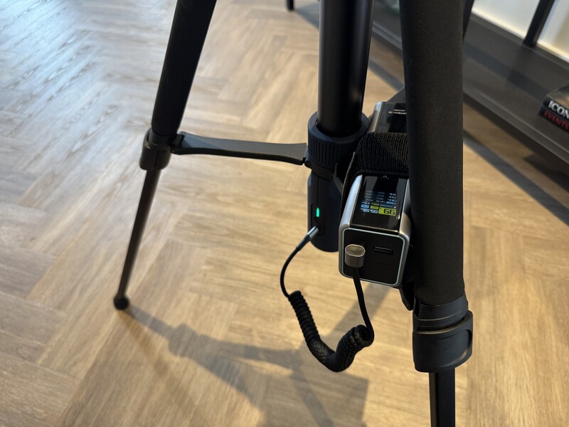 Close-up of a digital light meter mounted to a tripod leg with a wrist strap attachment.