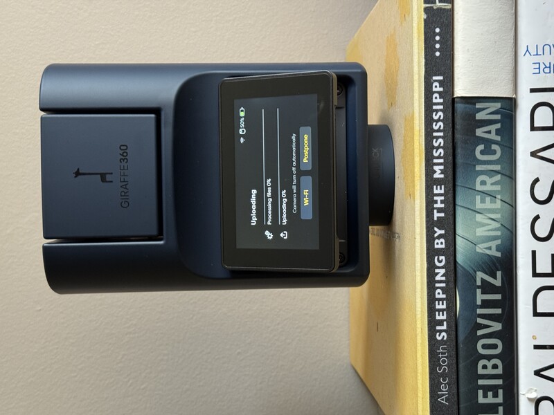 Square Point-of-sale payment terminal displaying uploading status on screen, sitting on stack of books.