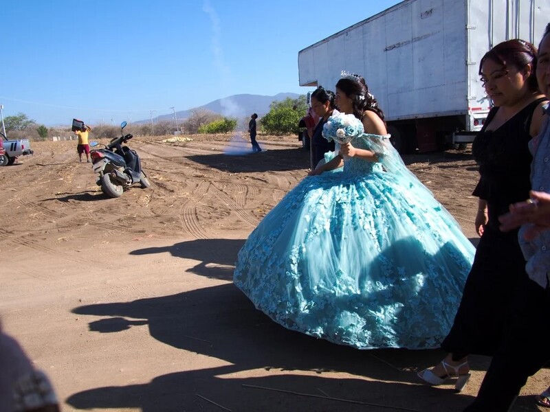 Woman in turquoise ball gown poses for camera in dusty outdoor setting with truck and mountains visible.