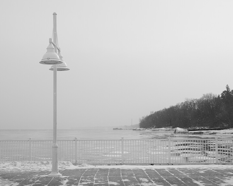 Black and white photograph of a lamp post on a lakefront pier