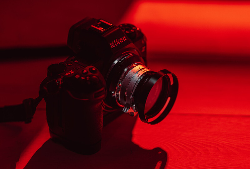 Nikon DSLR camera with attached lens, photographed against a red backdrop with dramatic lighting.