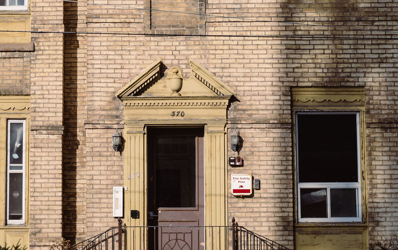 Brick facade of a historic building with a centered entrance featuring classical columns and a pediment.