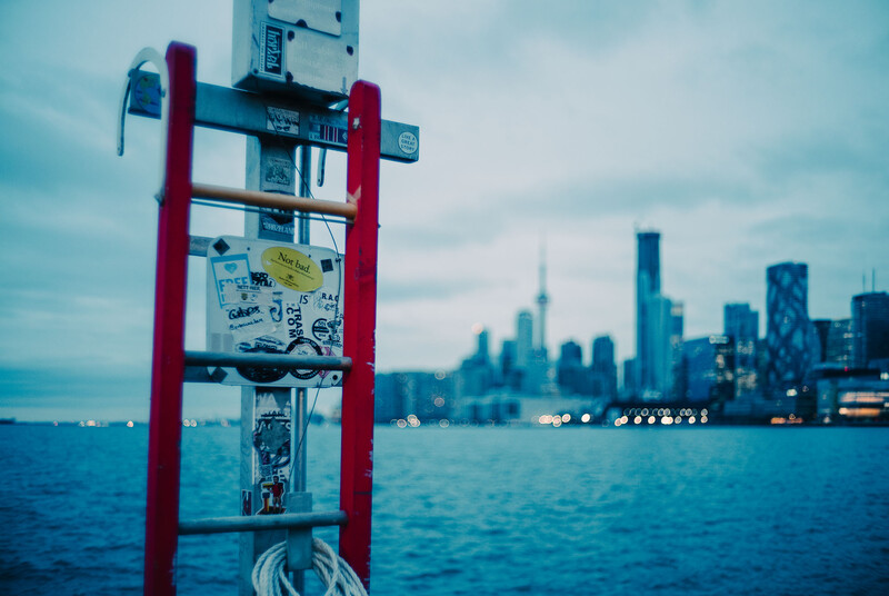 Red metal structure with utility equipment in foreground, city skyline across blue water in soft focus background.