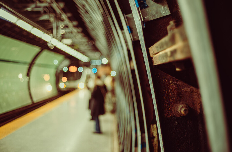 Blurred subway platform view from inside a train car, showing bokeh lights and a lone figure on the platform.