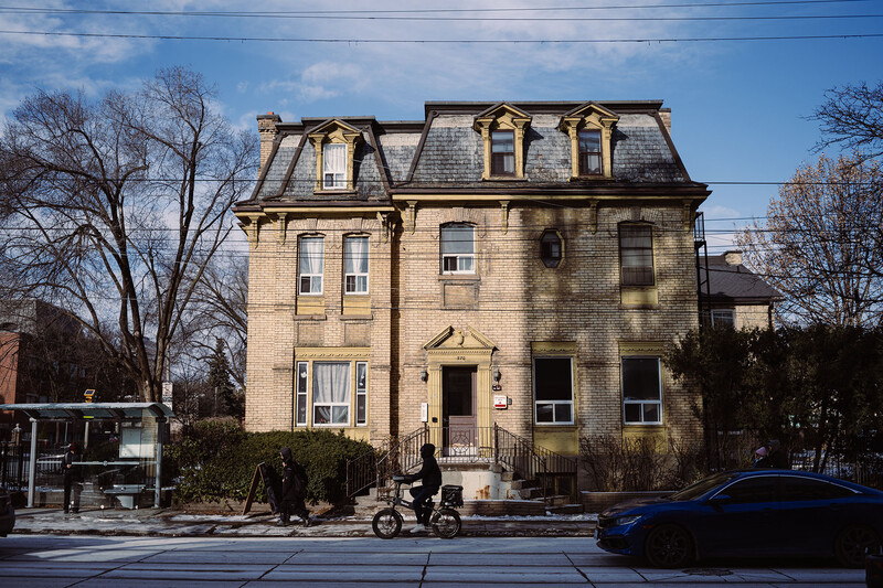 Yellow Second Empire mansion with mansard roof and dormer windows on a residential street.