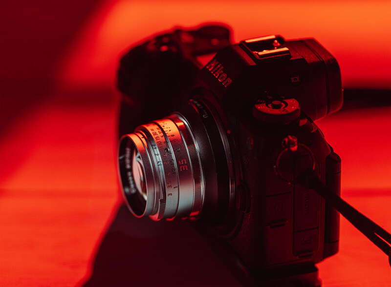 Mirrorless camera with prime lens against warm red and orange studio lighting backdrop.