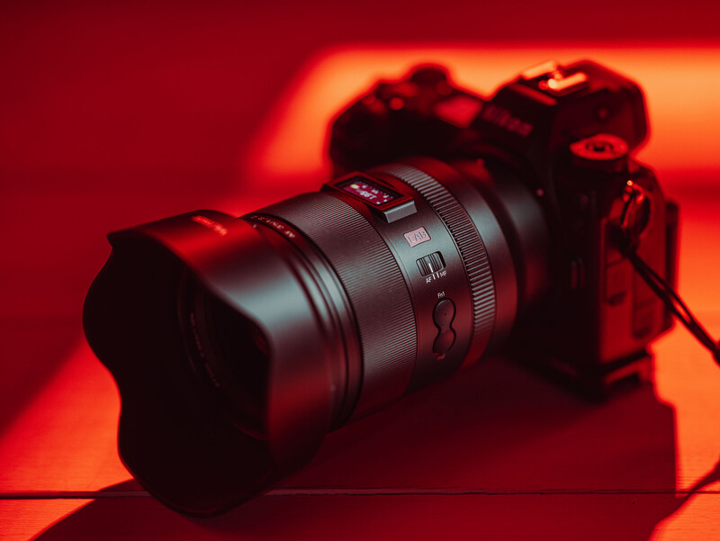 Mirrorless camera with telephoto lens on warm red-orange backdrop with dramatic lighting.