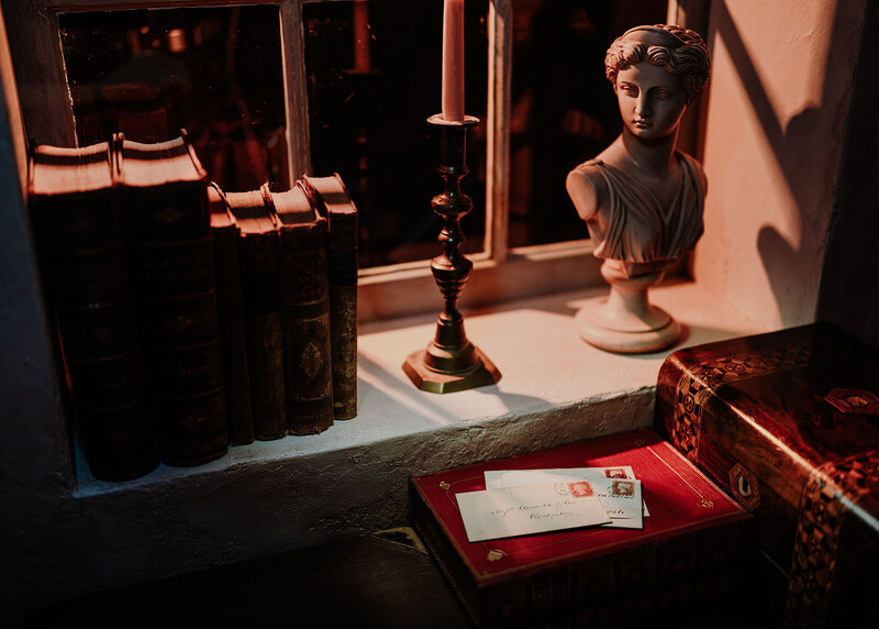 Still life arrangement with classical bust, candlestick, and red envelope on table with warm directional lighting.