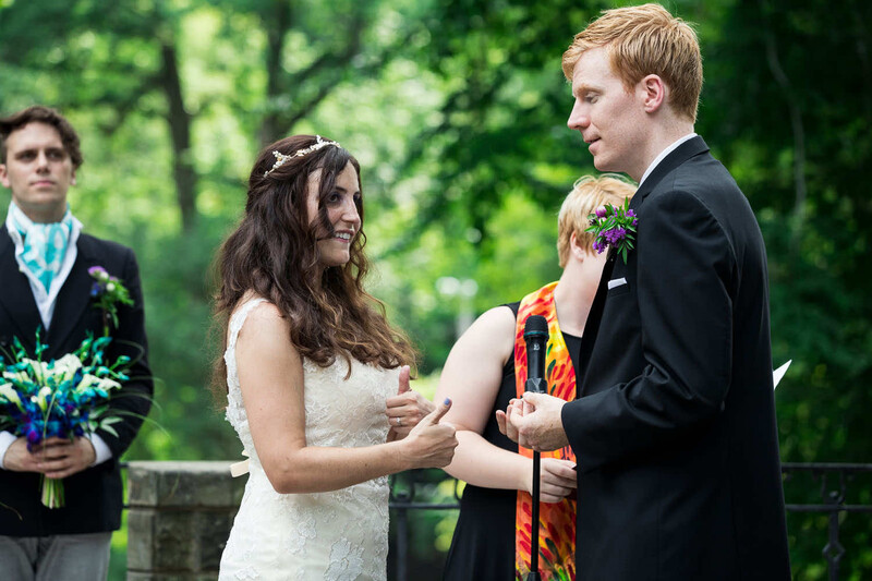 Bride and groom exchange vows during outdoor wedding ceremony with officiant and groomsman present.