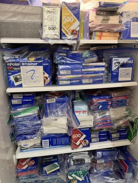 Shelving unit packed with photography equipment and supplies in blue packaging and storage boxes.