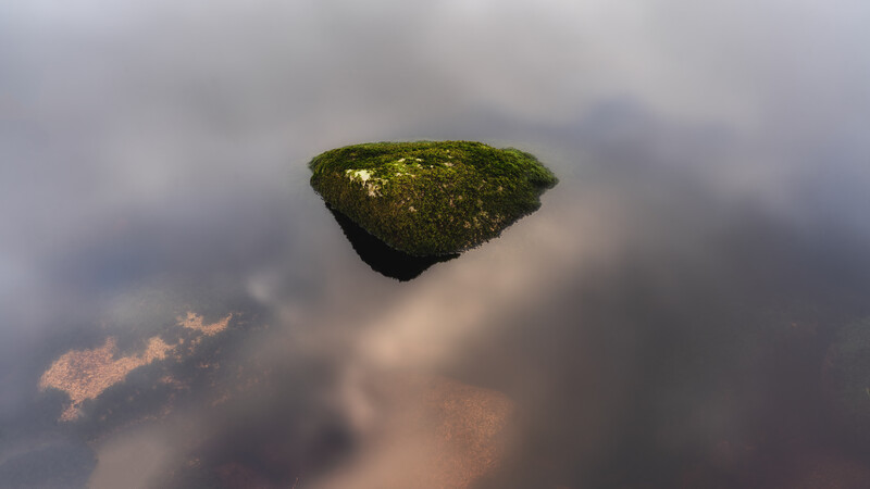 A long stone in water with reflective clouds