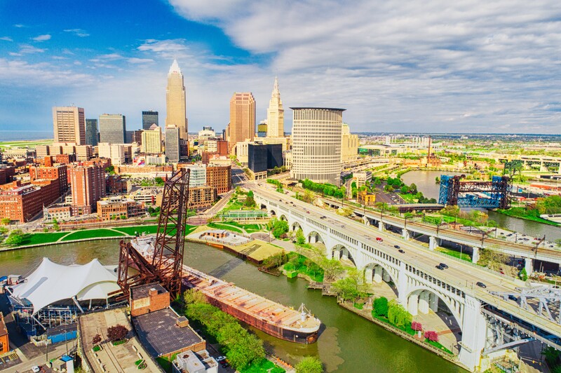 Urban skyline with tall buildings along a riverfront, featuring a historic lift bridge and industrial waterfront structures.