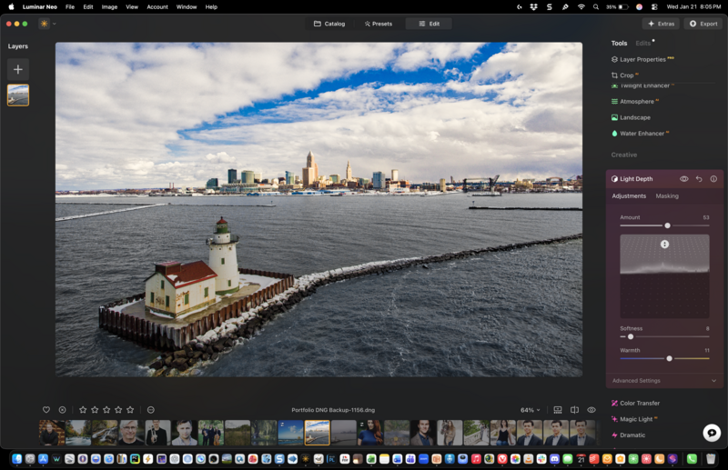 Lighthouse on a pier extending into calm water with city skyline and dramatic blue sky in background.