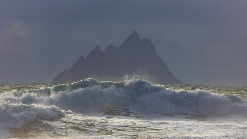 Dramatic seascape with large crashing waves and jagged dark rock formation rising from misty ocean.