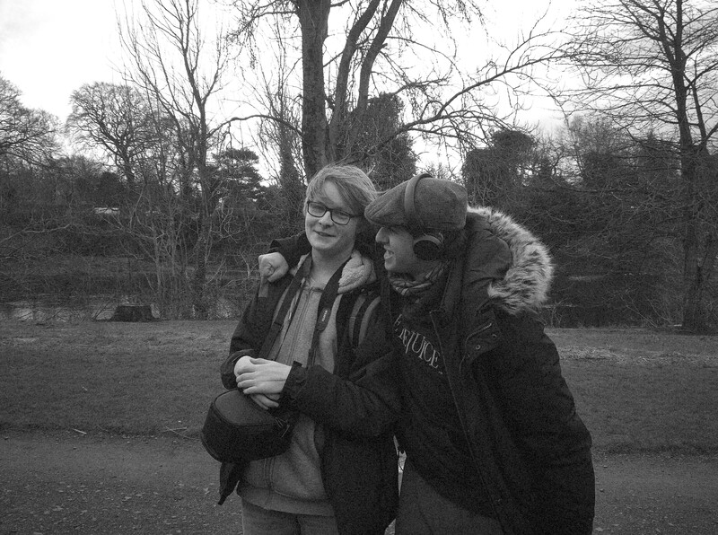 Three people posing together in a park, shot in black and white with bare trees in the background.