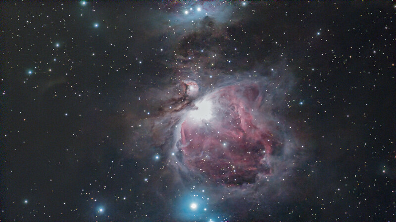 The Orion Nebula glows with pink and blue gas clouds surrounding bright central stars against a starfield.