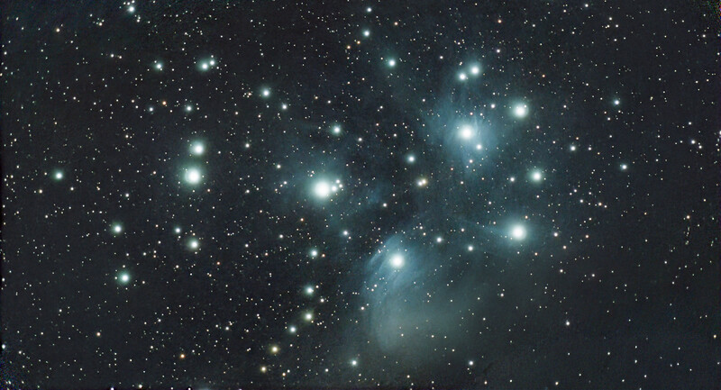 The Pleiades star cluster against a dark starfield, with bright blue-white stars and wispy nebulosity.