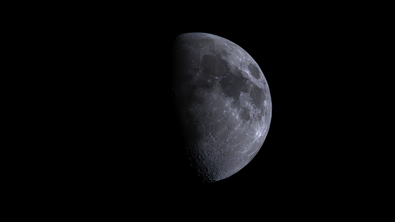 Half-illuminated moon against black space, showing detailed crater and surface texture on the lit side.