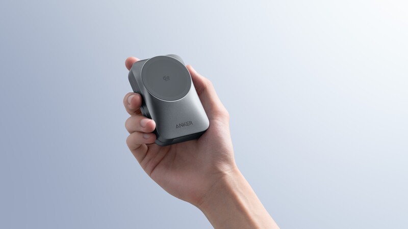 Hand holding a compact gray camera or imaging device against a light blue background.