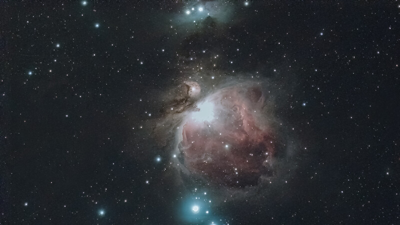 The Orion Nebula, a vast cloud of gas and dust illuminated by bright central stars against the black void of space.