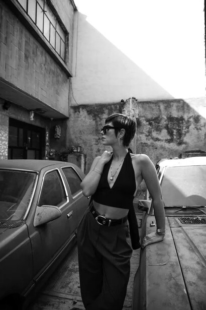 Woman in black sleeveless top and pants standing in parking garage with vintage cars in background.