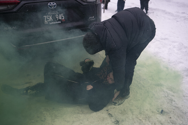 Person crouching beside a Toyota vehicle in snowy conditions, examining the undercarriage in low-light conditions.