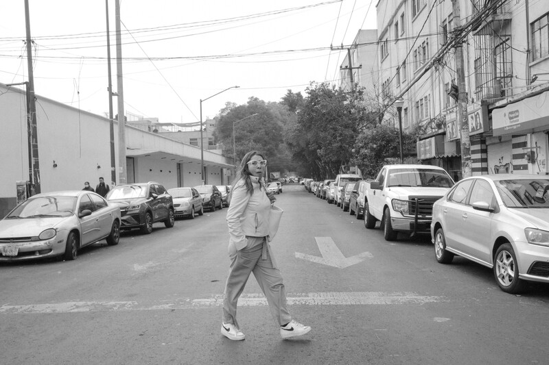 Woman standing in center of urban street lined with parked cars, shot in black and white.