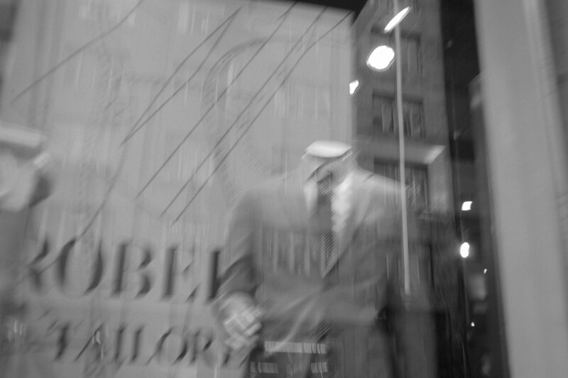 Black and white photograph of a storefront window with motion blur and rain streaks obscuring the view.
