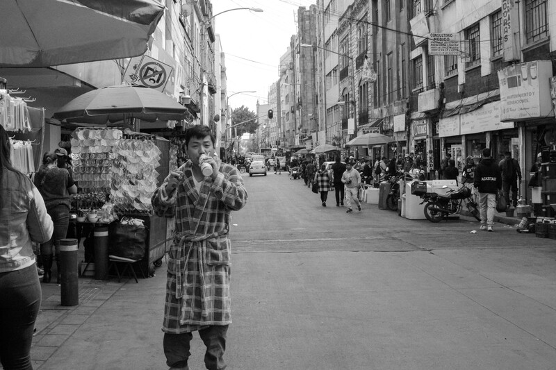 Person in checkered coat walking down a pedestrian shopping street lined with storefronts and other shoppers.