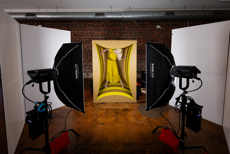 Professional studio setup with symmetrical softbox lighting, backdrop frame, and reflectors on wooden floor against brick wall.
