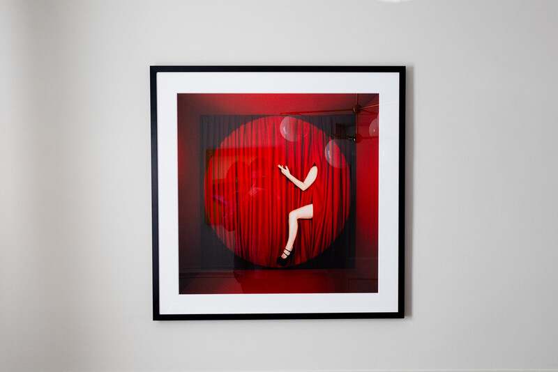 White stick figure sitting inside a large red sphere displayed in a black frame on white wall.