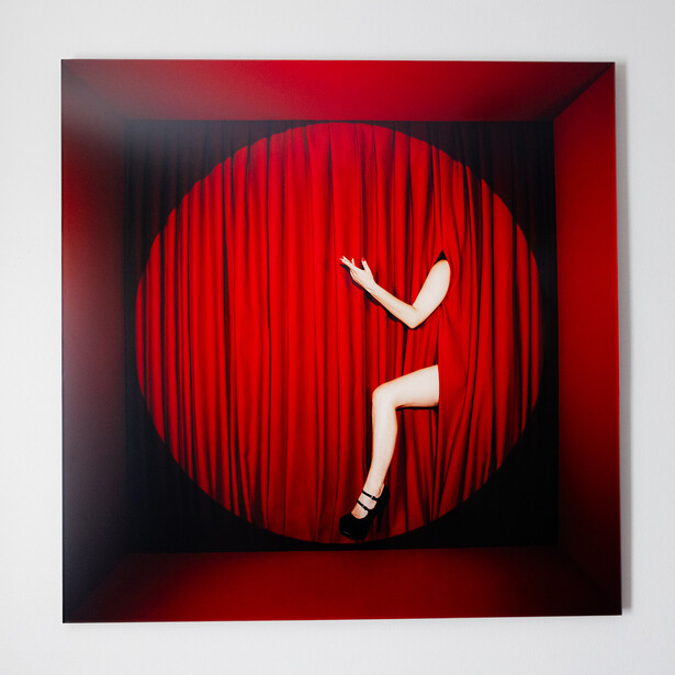 Illustration of a figure in white against a large red circular backdrop with vertical line texture, posed inside a dark geometric frame.
