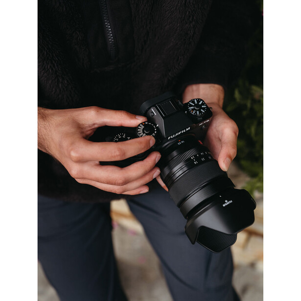 Photographer holding a mirrorless camera with telephoto lens during daytime outdoor shoot.