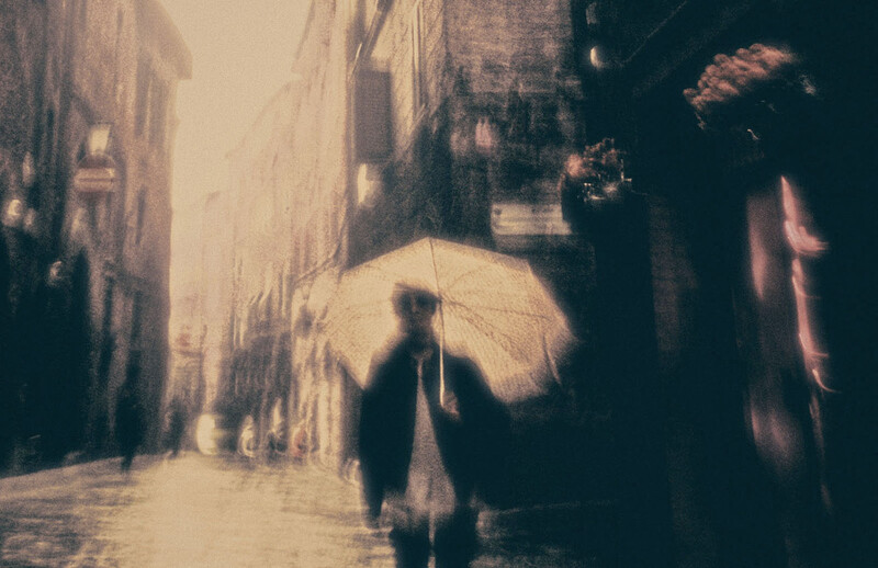 Figure holding white umbrella in narrow urban alleyway with soft, diffused light.