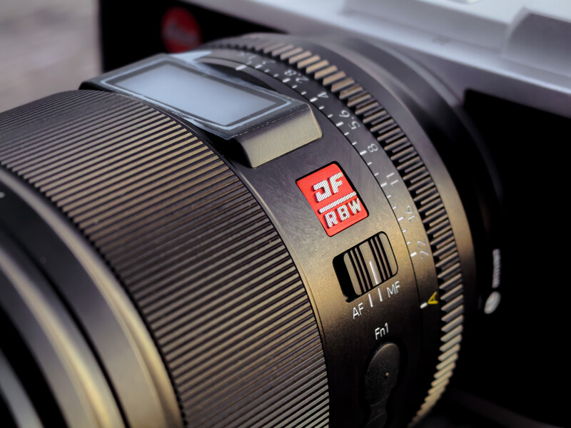 Close-up of a camera lens barrel showing focus ring, distance scale, and red AF/MF autofocus toggle switch.