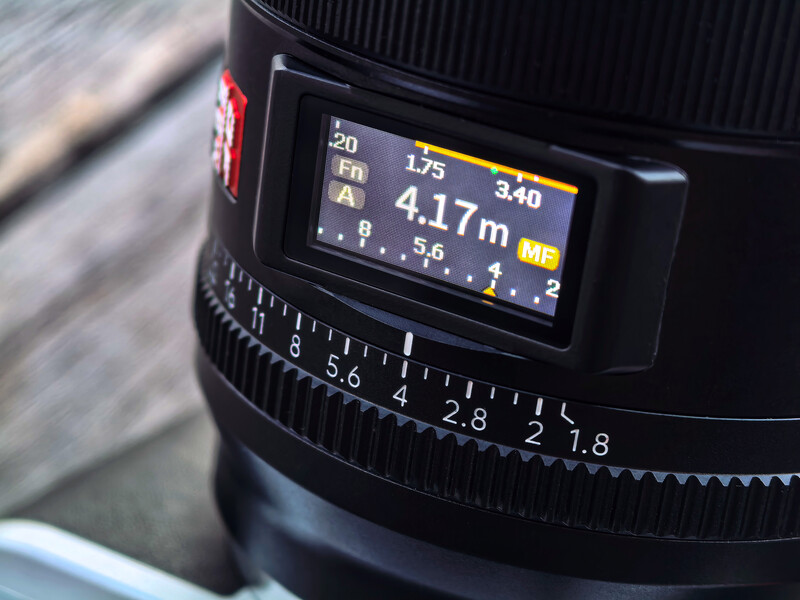 Close-up of a camera lens with digital display showing focal length and distance measurements.