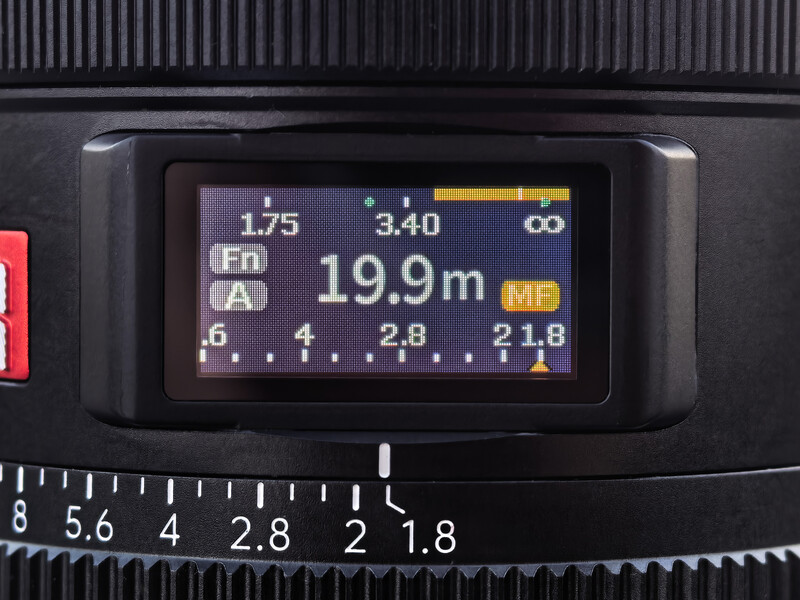LCD display on a camera lens showing focus distance of 19.9m and depth of field scale markings.