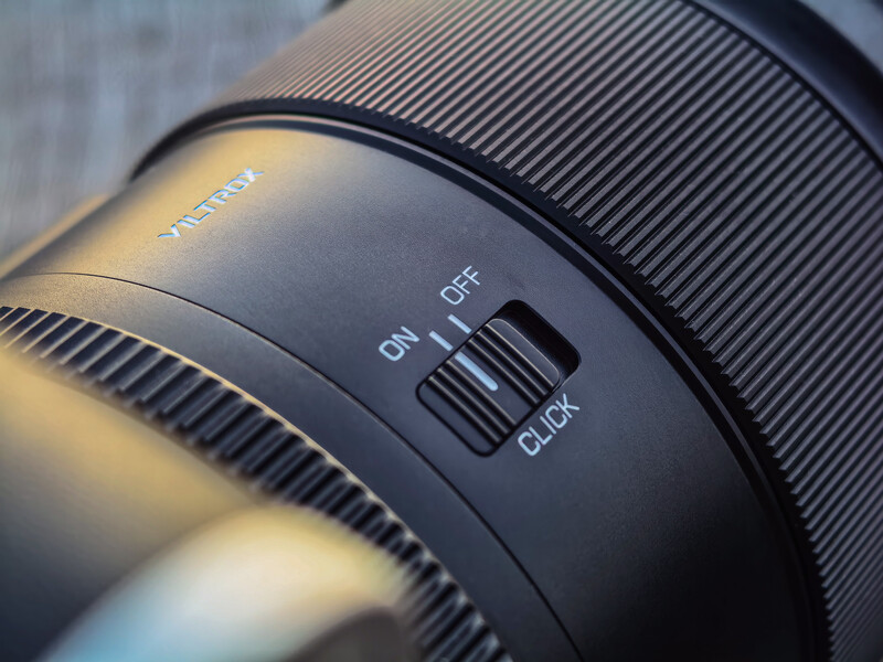 Close-up of camera lens showing focus ring, distance scale markings, and autofocus/manual focus switch.